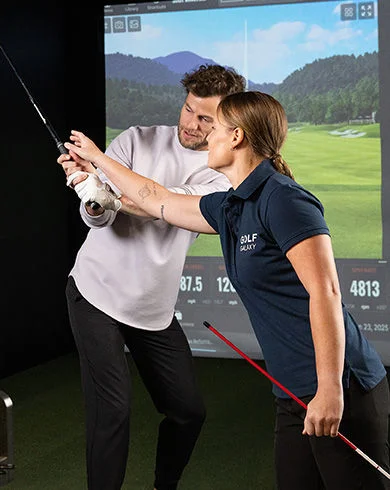 A golf instructor helps a student adjust his swing inside an indoor golf simulator. 
