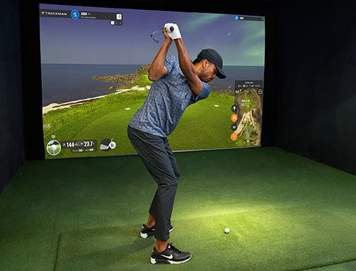 A golfer in front of a golf simulator screen.