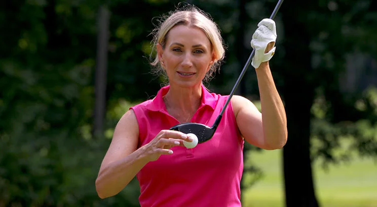 woman holding ball and tee talking to camera
